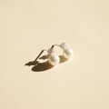 Pair of pearl earrings with diamond accents on a beige background