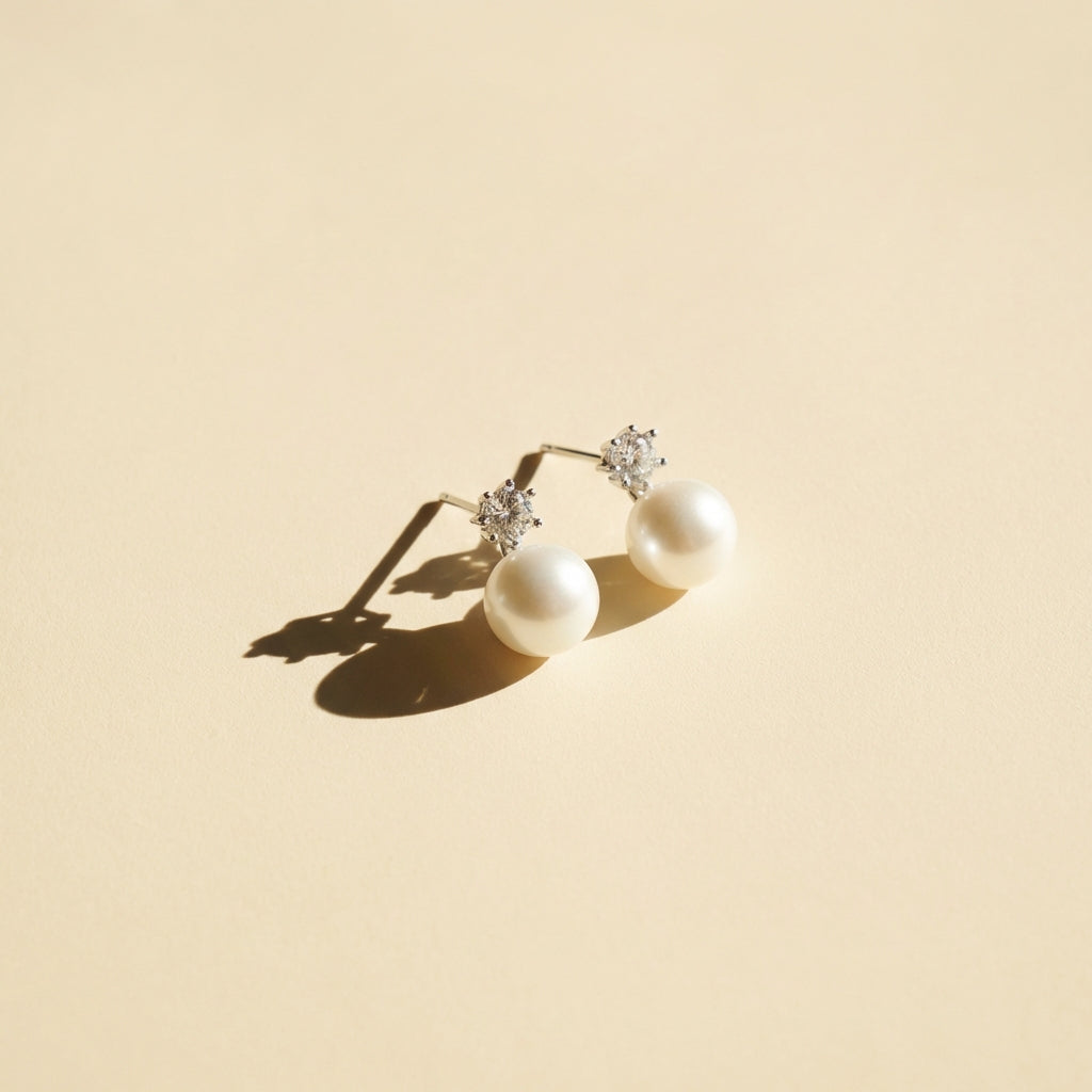Pair of pearl earrings with diamond accents on a beige background